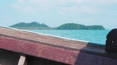 Sahildeki tropikal bir adaya doğru okyanus manzaralı bir yolculuk, arka planda yeşil bir adayla birlikte yıpranmış bir tekne, pitoresk deniz üzerinde sürüklenir. Tayland sahili macerası için mükemmel bir sahne..
