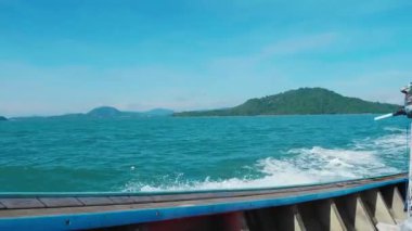 Tahta tekne, Tayland kıyısı boyunca turkuaz sularda yüzüyor. Okyanusun ortasındaki küçük vahşi adaları gösteriyor. Turistler tropikal gölde yüzmek için yelkenli kullanıyorlar..