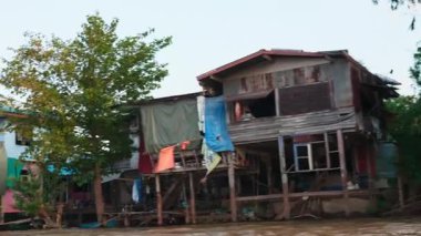 Günbatımında Tayland 'ın ünlü nehrinde yüzen turist yelkenlisi. Teknelerin kanal sularında yüzdüğü büyülü gece ulaşım deneyimi. Tayland köyü evleri ve manzarası.