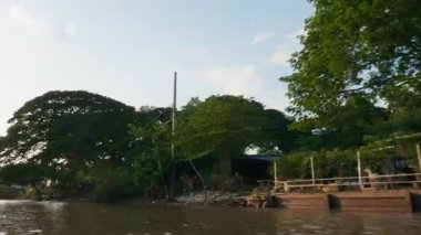 Günbatımında Bangkok 'un ünlü nehrinde yüzen turist teknesi. Teknelerin kanal sularında yüzdüğü büyülü gece ulaşımı deneyimi. Tayland köyü evleri ve manzarası.