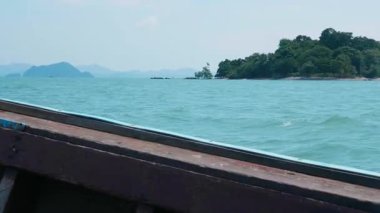 Geleneksel Tayland teknesi turkuvaz dalgalı açık denizde, tropikal sularda yüzen tekne tenha bir adaya doğru hareket ediyor, manzaralı deniz manzarası ve yaz tatilleri sergiliyor..