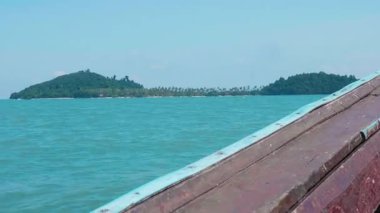 Tahta yelkenli ve yeşil adalı tropik deniz manzarası. Ufukta parlak yeşillikleri olan güzel bir ada. Geleneksel bir Tayland teknesi kristal berrak suları aşıyor..