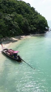 Tayland adası yakınlarındaki tropikal sulara demir atmış bir teknenin dikey video görüntüsü. Mavi suları ve egzotik kıyıları olan beyaz dalgalar yaratan bir teknenin yaz macerası.