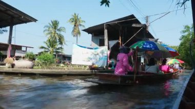 Tayland, Kasım 2024 - Teknelerle gezen turist grubu kanaldaki yelkenli teknelerinde otururken pazardan ürün ve geleneksel egzotik Tayland yemekleri satın almak için yüzer pazeyi ziyaret ediyor.