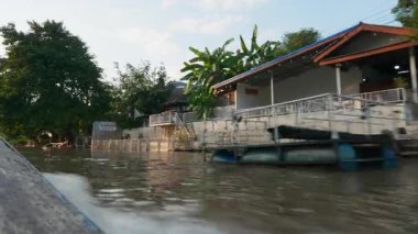Manzaralı yansımaları olan bir nehirde geleneksel Tayland yelkenlisi. Kanal boyunca ağaçlar ve binalarla yüzen ahşap bir teknenin bulunduğu güzel bir seyahat noktası..