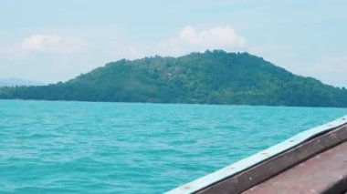 Turistler, tropikal sahil şeridi boyunca huzurlu tekne yolculuğunun tadını çıkarıyorlar. Durgun turkuaz okyanusta hareket eden tahta yelkenli sahil kayalıkları, kumlu plajlar ve el değmemiş bir gökyüzü sunuyor..