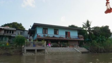 Nehir kanalında turistlerle birlikte yüzen Tayland yelkenlisi mavi sularda yüzen bir yelkenli ve yakındaki tropikal gökyüzü ve manzaralı bir köyde güzel bir nehir manzarası..