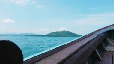 Geleneksel Tayland teknesi turkuvaz dalgalı açık denizde, tropikal sularda yüzen tekne tenha bir adaya doğru hareket ediyor, manzaralı deniz manzarası ve yaz tatilleri sergiliyor..