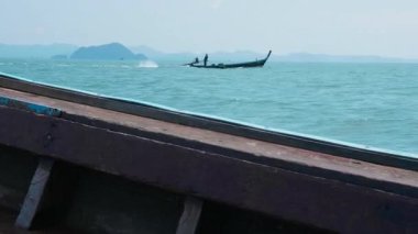 Sahil şeridi boyunca sakin mavi bir deniz üzerinde kırsal ahşap bir tekne okyanusta süzülüyor, büyüleyici bir Tayland lagünü manzarası sunuyor, yemyeşil adalar ve el değmemiş tropikal bir manzara..