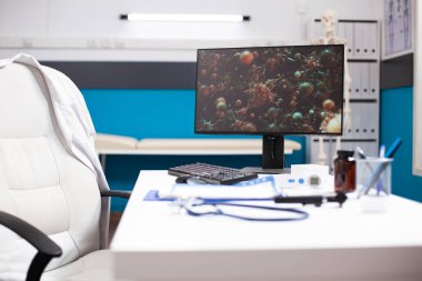 Modern klinik ofisi boş duruyor ve masaüstü monitörü biyoloji araştırmaları için virüs hücrelerini gösteriyor. Kontrolsüz doktorlar masası ve teknoloji hastalıklara karşı tıbbi bilimde devam eden çabaları yansıtıyor.