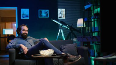 Komik komedi filmi izlerken koltukta oturup gülen, patlamış mısır yiyen eğlenceli bir adam. Apartmandaki neşeli insan abur cubur yiyor ve film sahnesinde komik bir şakayla eğleniyor, kamera B