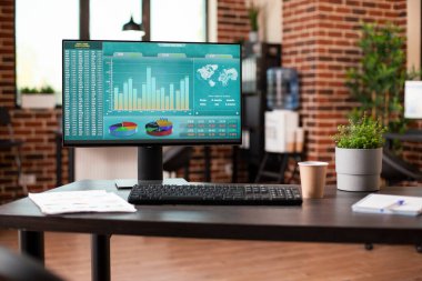 Boş tuğla duvar odası bilgisayar monitörünü gösteriyor. Finansal analiz sonuçları masaya konmuş. Evrak işleri ve kahve de yakınlarda. Başlangıç ofisi kurulumu verimli ve doğru şirket araştırmalarını destekler.