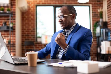 Başlangıç ofisindeki erkek analist önemli bir iş anlaşmasını sonuçlandırdıktan sonra sevindi. Siyah işadamı dizüstü bilgisayardaki proje sunumuyla ilgili olumlu sonuçları okuduktan sonra sevinçle yumruğunu kaldırdı.