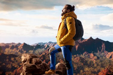 Zirvede duran kararlı dağcı huzurlu bir başarı anının tadını çıkarıyor. Uçsuz bucaksız gökyüzü, sıradağlar ve temiz hava özgürlüğün, refahın ve keşiflerin özünü vurguluyor..