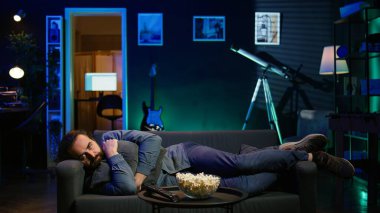 Yastığa uzanmış televizyon seyreden adam, üzgün bir film senaryosuyla kalbi kırılmış. Üzgün izleyiciler, RGB 'nin aydınlattığı dairedeki kanepeye uzandı. İç karartıcı televizyon şovu sahnesi, B kamerasından rahatsız oldu.