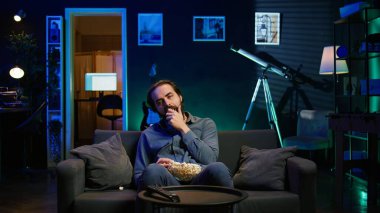 Yorgun adam gece geç saatlerde TV 'de program izliyor ve patlamış mısır yiyor, ekrana dikkatle bakıyor. Bütün gün pijamayla oturan yorgun bir adam akılsızca eğleniyor, kamera B