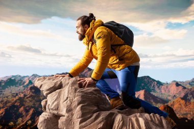 Doğa aşığı nefes kesen bir dağ sırasının kenarında duruyor, yükselen zirvelerin ve uçsuz bucaksız gökyüzünün manzaralı arka planına bakıyor. Genç adam macera ve açık hava keşiflerini seviyor..