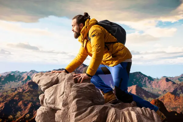 Doğa aşığı nefes kesen bir dağ sırasının kenarında duruyor, yükselen zirvelerin ve uçsuz bucaksız gökyüzünün manzaralı arka planına bakıyor. Genç adam macera ve açık hava keşiflerini seviyor..