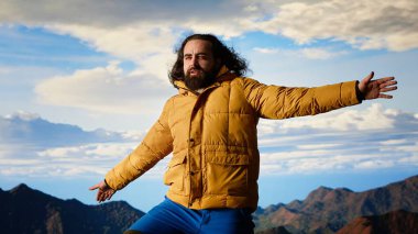 Mutlu maceracı dağın tepesinde olmanın heyecanını kucaklıyor, başarının gücünü hissediyor. Huzurlu gökyüzü ve uçsuz bucaksız vahşi doğası ile ilham verici bir dağ sırası. Kamera B.