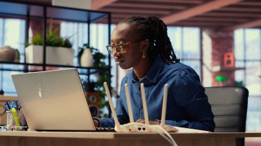 Evdeki siyahi kadın modemi ve sorun çözme rehberini inceliyor, kablosuz ağ yönlendiricisini tamir etmeye çalışıyor ve uzak bağımsız işler için internet bağlantısını onarmaya çalışıyor. Sinyal kaybı. Kamera B.