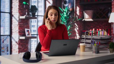 Ev ofisinin çatı katında bilgisayarla çalışırken cep telefonuyla konuşan odaklanmış bir kadın. Görevleri çözmek için iletişim becerileri ve yaratıcılığı kullanarak çağrılarla, toplantılarla ve soruşturmalarla uğraşıyor. Kamera B.