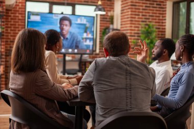 Beyaz adam ve meslektaşları toplantı odasında görüntülenen sanal müşteri sunumunu dikkatle dinliyorlar. Siyahi yöneticilerle birlikte video üzerinde beyin fırtınası yapan iş adamları.