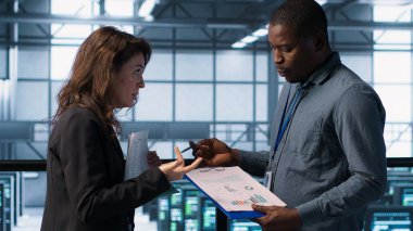 Veri merkezi ekibi sunucu odasındaki evrak dosyalarını inceliyor, sistem tanılarını inceliyor. Sunucu odası çalışanları bakım çizelgelerini ve siber güvenlik protokollerini inceliyor. Kamera A