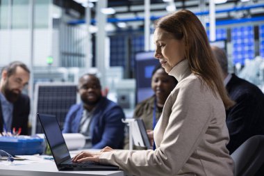 Photovoltaics fabrika yönetimi ekibi dizüstü bilgisayarları kullanarak verileri analiz ediyor, sistem sağlık ölçümlerini gözden geçiriyor. Güneş panelleri imalat tesisi yöneticileri dizüstü bilgisayar kullanarak teknik sorunları çözüyorlar