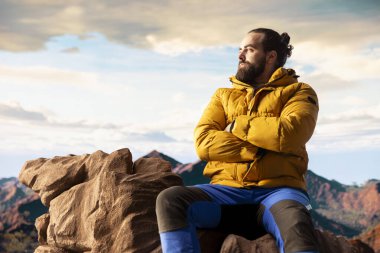 Yürüyüş yolcusu, tepedeki panoramik dağ manzarasına, sonsuz gökyüzüne ve kayalık tepelere hayranlık duymak için ara verir. Zihinsel berraklık için nefes kesici bir zemin oluşturur. Dışarıdaki maceracı..