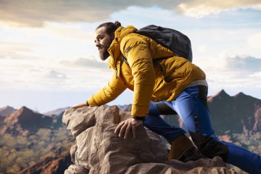 Kararlı gezgin, panoramik manzaranın macera ve kişisel gelişimi temsil ettiği bir dağ zirvesinin yalnızlığının tadını çıkarıyor. Açık hava teçhizatıyla yürüyüşçü rüzgarlı dağın tepesinde üşüyor..