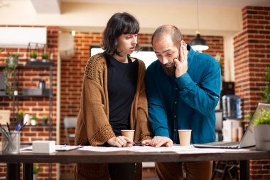 Kafkasyalı meslektaşlar telefonda müşteriyle aktif olarak iş projesini tartışıyor. İş adamı şirket araştırma belgelerini ofis masasında çalışan bir bayanla birlikte gözden geçirirken mobil cihazla konuşuyor..