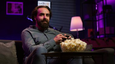 Neşeli oyuncu kanepede oturmuş oyun konsolu ve oyun sahası kullanarak online çok oyunculu turnuvaya katılıyor. Neşeli oyuncu eğlenceli video oyunlarıyla meşgul, boş zamanların tadını çıkarıyor, kamera A