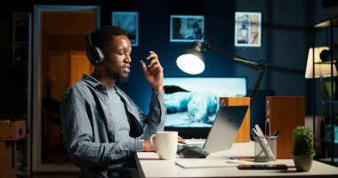 Afrika kökenli Amerikalı bir adam iş arkadaşlarıyla video bağlantısına el sallıyor, evinden uzaktan çalışıyor ve idari toplantılara katılıyor. Sanal iletişim. Kamera A.