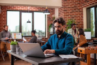 Diz üstü bilgisayarında, tuğladan duvar çalışma alanı gibi bir iş stratejisinde oturan erkek çalışan, yeni başlayan şirketlerin finansal ve pazarlama planlarına odaklanıyor. Şirket araştırması yapan girişimci..