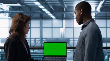 Bilgisayar bilimcilerinden oluşan veri merkezi ekibi ekipman teşhislerini gözden geçirmek için laptop kullanıyor. Ekip çalışması bilişim uzmanları sunucu odası ayarlarını kroma anahtar defteri, kamera A kullanarak ayarlıyorlar.