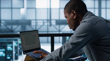 Veri merkezinde bilgisayar kullanan, güç yönetimi ayarlarını ayarlayan, programlama dilleri kullanan bir teknisyen. Sunucu odasındaki adam kaynak kullanımını optimize ediyor, istikrarlı altyapıyı koruyor, kamera A