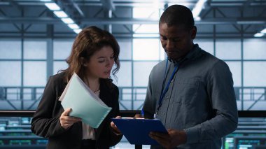 Veri Merkezi yöneticileri evrak dosyalarını okuyor, sistem tanılarını gözden geçiriyorlar. Sunucu çiftliği meslektaşları bakım takvimlerini evrakları ve siber güvenlik protokollerini inceliyor, kamera A