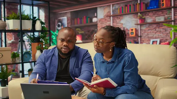 Yetişkin insanlar sehpada program ve planlama faaliyetlerini denetliyor, online araçlarla zaman yönetimi üzerinde çalışıyor. Defter kullanan ve el yazısı notlar alan bir çift. Kamera A.