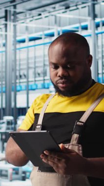 Dikey video akıllı fabrika mühendisi tesis katındaki robot silah ve montaj hatlarını denetliyor. Endüstri 4.0 Afro-Amerikan erkeği sistem performansını ve sorunlarını izliyor