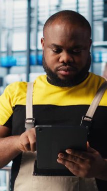 Dikey video akıllı fabrika mühendisi tesis katındaki robot silah ve montaj hatlarını denetliyor. Endüstri 4.0 Afro-Amerikan erkeği sistem performansını ve sorunlarını izliyor