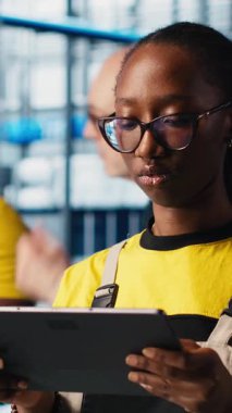 Dikey video endüstrisi 4.0 bitki teknisyeni dijital cihaz uygulaması kullanılarak sistem performansını gözlemler. Akıllı fabrika mühendisi, tablet üzerindeki yazılımı kullanarak robotik silah ve taşıma bantlarının çalışmasını denetliyor.