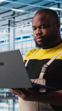 Sektör 4.0 endüstriyel fabrikadaki gülen mühendis bilgisayarla otomatik makineleri kontrol ederek iş akışının devamlılığını sağlıyor. Mutlu akıllı fabrika teknisyeni robot kolları kullanıyor.