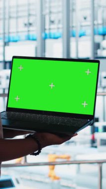 Akıllı fabrikada yeşil ekran dizüstü bilgisayar kullanan dikey video işçisi veri toplayıp analiz ediyor. Gelişmiş teknolojiyle donatılmış endüstriyel santralde krom anahtar defteri üzerinde izleme yazılımı kullanan uzman