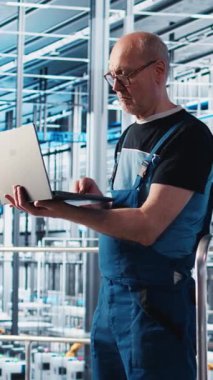 Dikey video mühendisi, otomatik sistemleri test etmek ve güvenilirliği sağlamak için akıllı fabrikada dizüstü bilgisayar kullanır. Deneyimli teknisyen, darboğazları tanımlamak ve ekipmanları optimize etmek için dizüstü bilgisayar kullanır