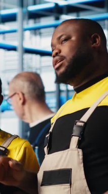 Dikey video Photovoltaics akıllı fabrika personeli tablet kullanarak PV materyallerini araştırıyor. Sanayi 4.0 güneş panelleri Afro-Amerikan mühendisleri alternatif enerji sistemleri geliştiriyor