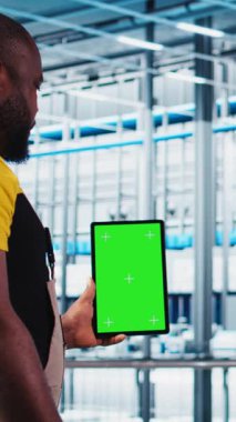 Otomatik sistemleri test etmek ve güvenilirliği sağlamak için yeşil ekran tableti kullanan dikey video akıllı fabrika uzmanı. İşçi, dar boğazları tanımlamak ve sensörlere dayalı donanımı optimize etmek için krom anahtar aygıtı kullanır