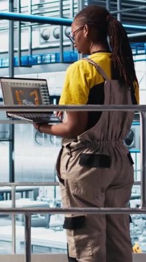 Fotovoltaik 'teki dikey video teknisyeni akıllı fabrikada dizüstü bilgisayar kullanarak veri analiz ediyor. Sektör 4.0 güneş panelleri uzmanı yenilenebilir enerji üreten tesis sistem ölçümlerini gözden geçirmek için defter kullanıyor