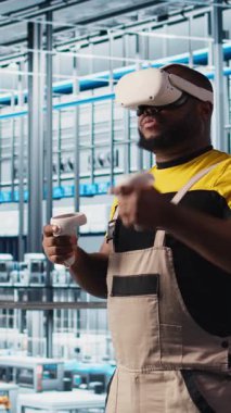 Dikey video akıllı fabrika mühendisi robotik silah ve taşıma bantlarının çalışmasını denetlemek için VR kulaklık kullanıyor. Sanayi 4.0 bitki teknisyeni sanal gerçeklik ve kamera kullanarak sistem performansını izler