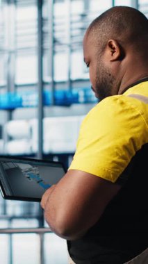 Dikey video endüstrisi 4.0 endüstriyel fabrika uzmanı tablet üzerindeki CAD programını kullanarak yeni robot makineler tasarlıyor. Afrika kökenli Amerikalı bir adam akıllı fabrikada otomasyon ekipmanları için cihaz kullanıyor.