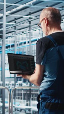 Dikey video akıllı fabrika uzmanı otomatik sistemleri test etmek ve güvenilirliği sağlamak için dizüstü bilgisayar yazılımı kullanıyor. İşçi, dizüstü bilgisayarda dar geçitleri tanımlamak ve sensörlere dayalı donanımı optimize etmek için program kullanır